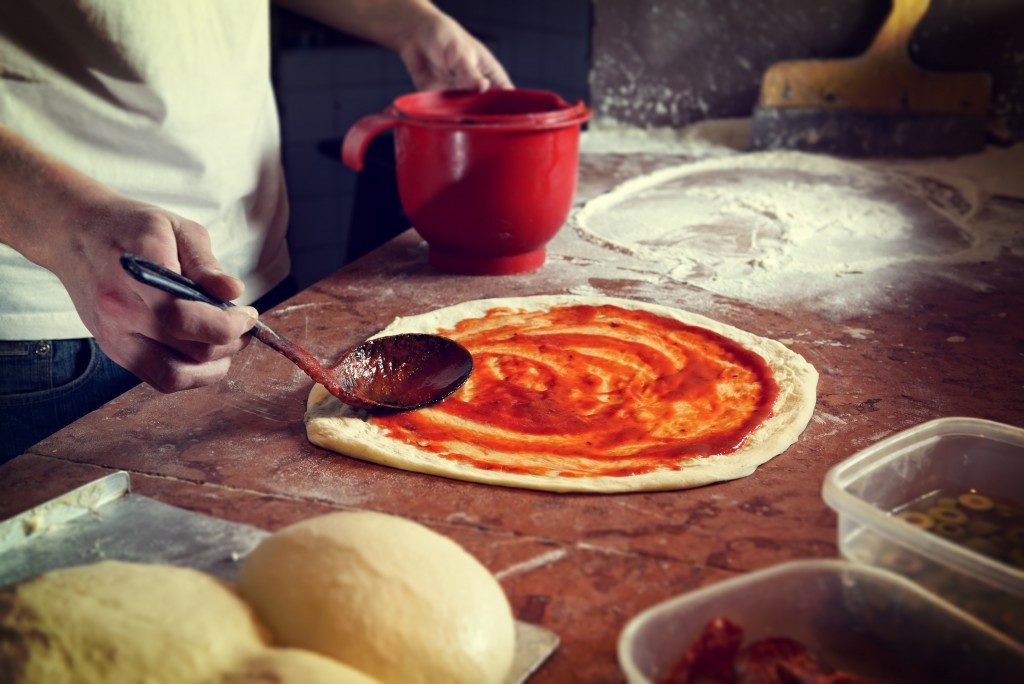 person putting sauce in dough